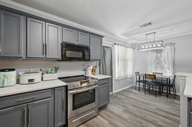 Kitchen with black microwave, stainless steel electric stove, gray cabinets, crown molding, and light countertops | Image 12