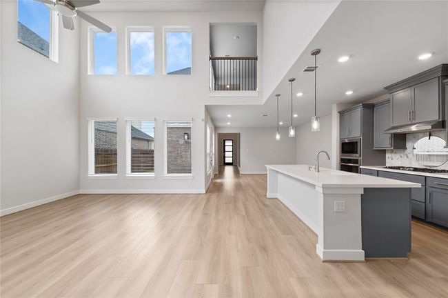 Spacious, light-filled living area featuring soaring ceilings, tall windows, and an open layout that flows seamlessly into a modern kitchen with quartz countertops, pendant lighting, and stylish gray cabinetry. | Image 8