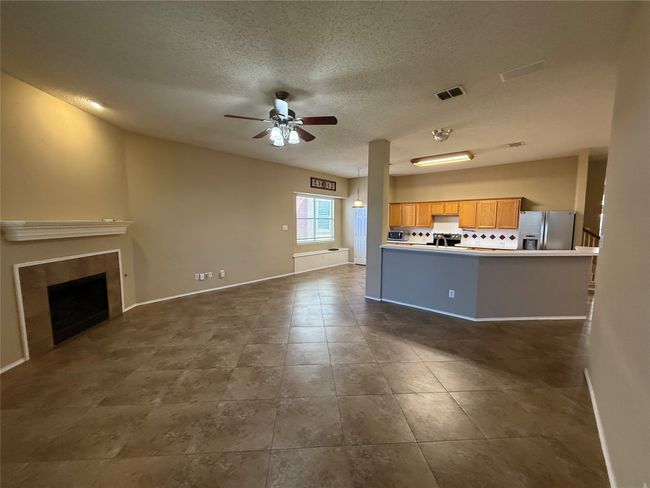 Living area with ceiling fan, a textured ceiling, a tiled fireplace, dark tile patterned floors, and baseboards | Image 7