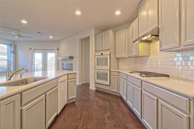 Kitchen with under cabinet range hood, white appliances, ceiling fan, light countertops, and decorative backsplash | Image 18