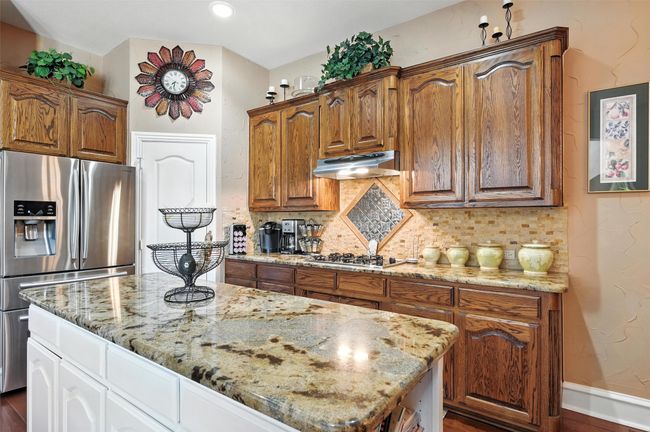Kitchen with stainless steel appliances, under cabinet range hood, light stone counters, tasteful backsplash, and a center island | Image 5