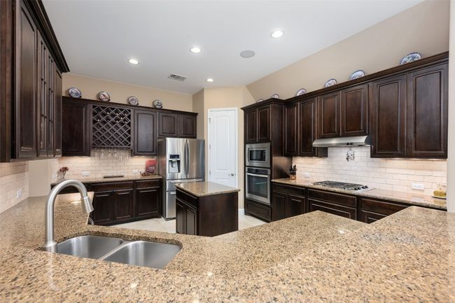 Kitchen with appliances with stainless steel finishes, under cabinet range hood, light stone counters, decorative backsplash, and dark brown cabinetry | Image 17