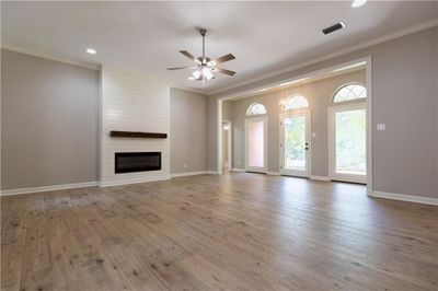 Unfurnished living room featuring hardwood / wood-style floors, crown molding, ceiling fan, and a large fireplace | Image 3