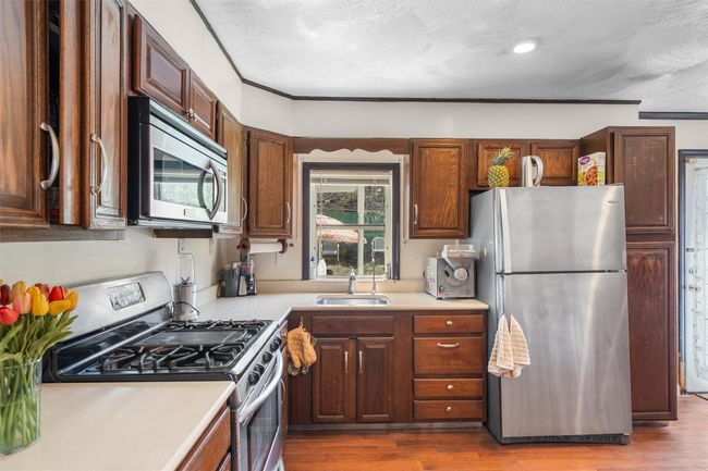 Kitchen with stainless steel appliances, a sink, light countertops, dark wood-style flooring, and ornamental molding | Image 7