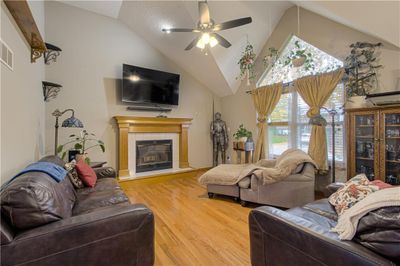 Living room featuring ceiling fan, wood-type flooring, a fireplace, and high vaulted ceiling | Image 2