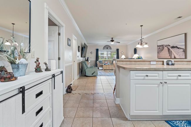 Kitchen with crown molding, white cabinets, a ceiling fan, light tile patterned flooring, and hanging light fixtures | Image 15
