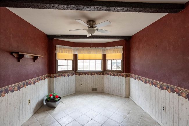 Unfurnished room featuring wallpapered walls, light tile patterned floors, a ceiling fan, wainscoting, and beamed ceiling | Image 9