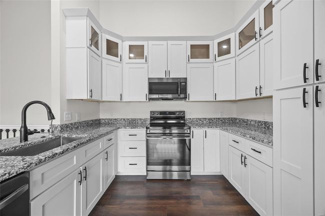 Kitchen featuring light stone countertops, dark wood-type flooring, white cabinets, a sink, and stainless steel appliances | Image 29