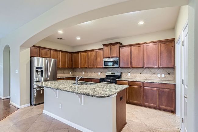 Kitchen with appliances with stainless steel finishes, arched walkways, light stone counters, backsplash, and a center island with sink | Image 11