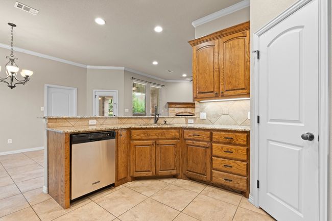 Kitchen with stainless steel dishwasher, crown molding, a peninsula, tasteful backsplash, and brown cabinetry | Image 15