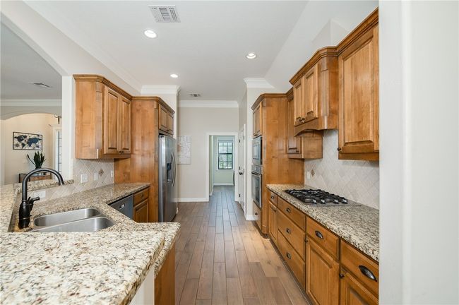 Kitchen featuring light stone counters, appliances with stainless steel finishes, a sink, baseboards, and visible vents | Image 11