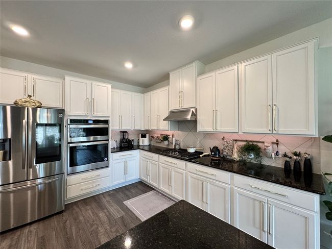 Kitchen featuring stainless steel appliances, under cabinet range hood, white cabinetry, tasteful backsplash, and dark wood-type flooring | Image 13