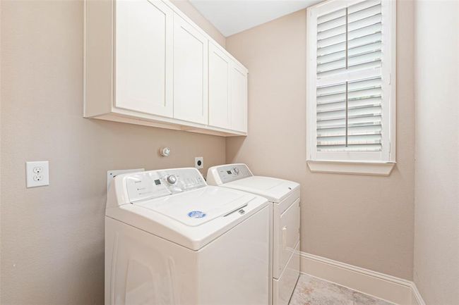 Dedicated laundry room with upper cabinet storage, full-size washer and dryer connections, tile flooring, and a window with plantation shutters for natural light and ventilation. | Image 23