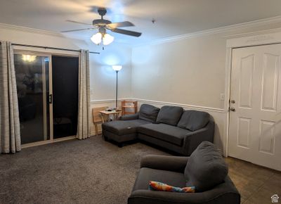 Living room with ceiling fan, crown molding, and dark colored carpet | Image 2