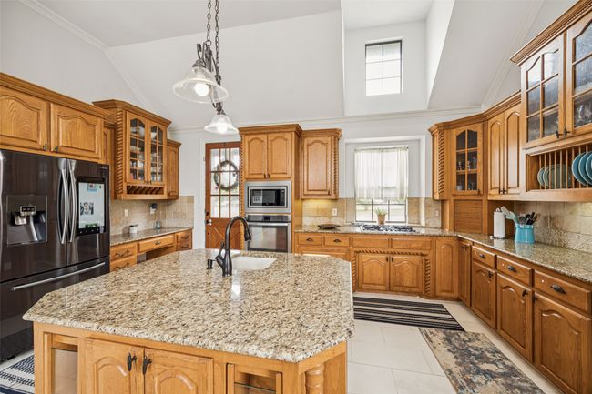 Kitchen with stainless steel appliances, plenty of natural light, a center island with sink, brown cabinetry, and crown molding | Image 7