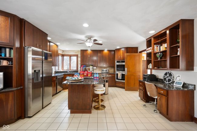 kitchen featuring built in study area, open shelves, appliances with stainless steel finishes, a kitchen breakfast bar, and a center island | Image 15
