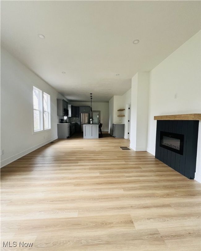 Unfurnished living room featuring light wood-type flooring, baseboards, a glass covered fireplace, and recessed lighting | Image 5
