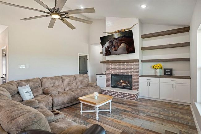 Living room with dark hardwood / wood-style floors, a fireplace, ceiling fan, high vaulted ceiling, and built in shelves | Image 8