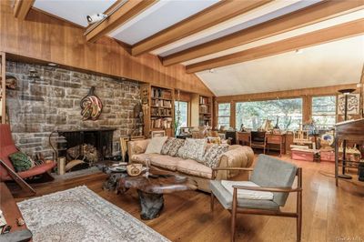 Living room featuring a stone fireplace, hardwood / wood-style flooring, wooden walls, lofted ceiling with beams, and built in shelves | Image 3