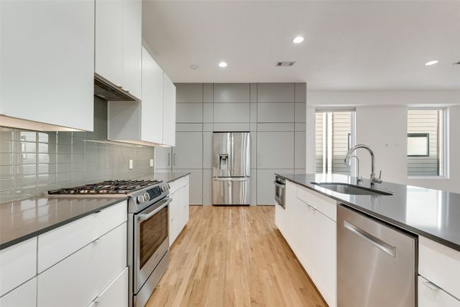Kitchen featuring appliances with stainless steel finishes, a sink, dark countertops, modern cabinets, and light wood floors | Image 12