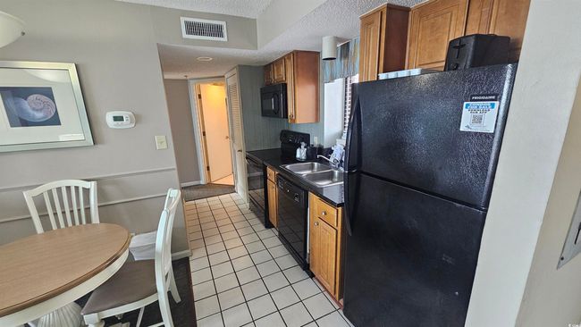Kitchen featuring light tile patterned floors, a textured ceiling, a sink, visible vents, and black appliances | Image 8