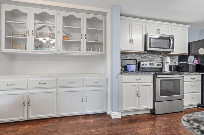 Kitchen featuring stainless steel appliances, white cabinets, glass insert cabinets, tasteful backsplash, and dark wood-style flooring | Image 11
