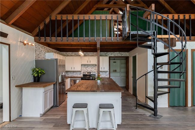 Kitchen with stainless steel appliances, butcher block countertops, wood finished floors, white cabinetry, and wooden ceiling | Image 5