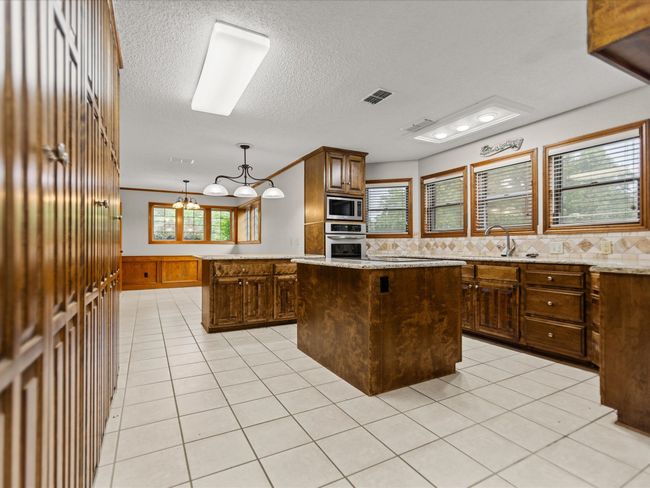 Kitchen featuring stainless steel appliances, a center island, a sink, light tile patterned floors, and a wainscoted wall | Image 17