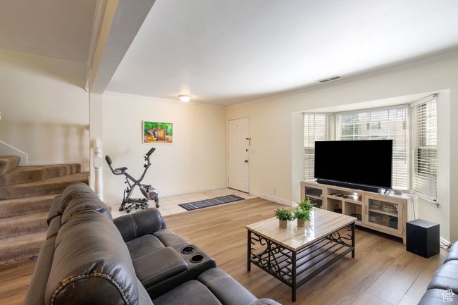 Living area featuring baseboards, crown molding, stairs, visible vents, and wood finished floors | Image 4