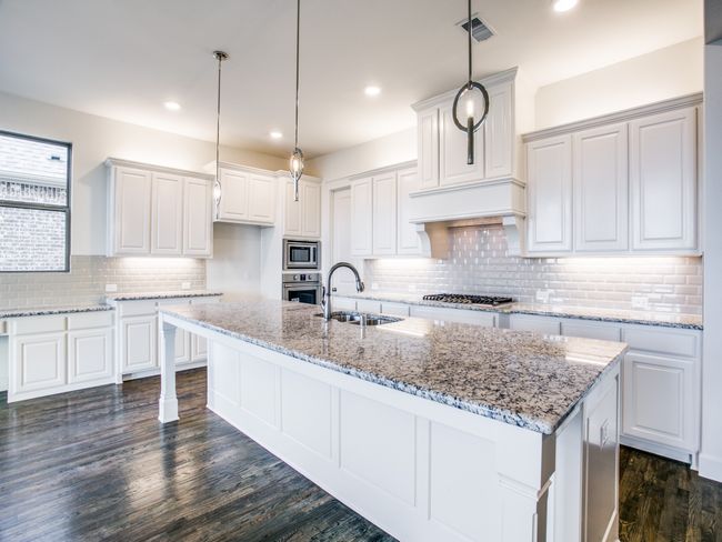Kitchen with appliances with stainless steel finishes, an island with sink, backsplash, dark wood-style floors, and white cabinets | Image 9