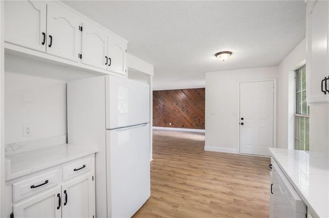 Kitchen with white appliances, wooden walls, white cabinets, light wood finished floors, and light stone countertops | Image 6