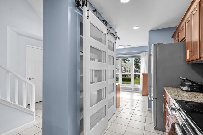 Kitchen with brown cabinets, a barn door, light tile patterned floors, recessed lighting, and light stone countertops | Image 9