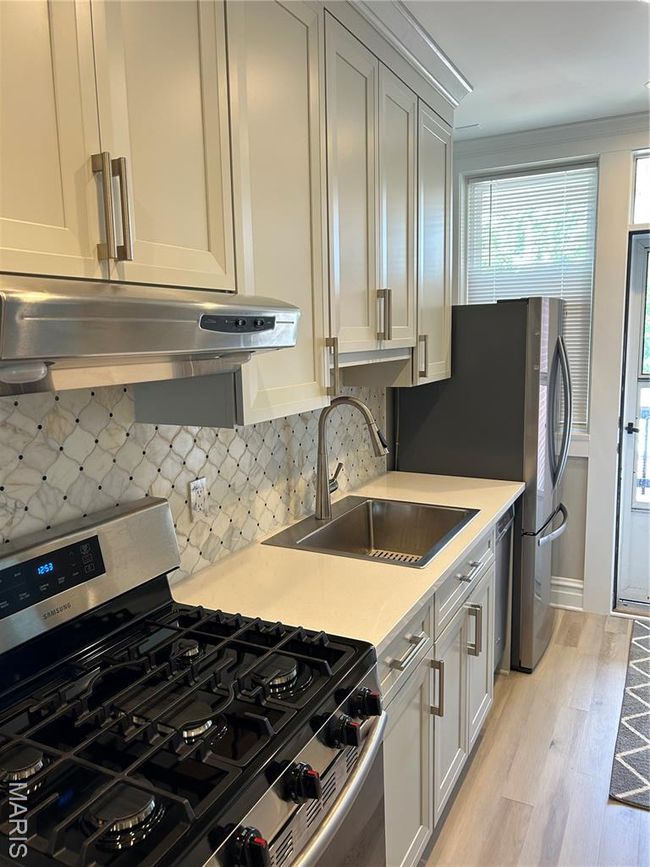 Kitchen with stove, extractor fan, light countertops, light wood-style flooring, and backsplash | Image 8