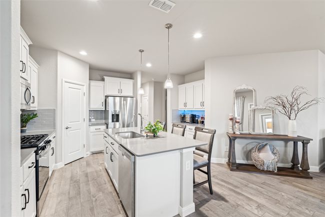 Kitchen with visible vents, light wood finished floors, a sink, stainless steel appliances, and a kitchen bar | Image 5