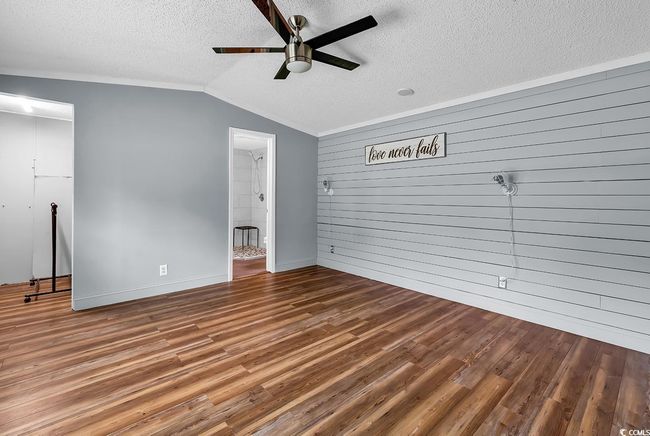 Empty room with ceiling fan, wooden walls, lofted ceiling, a textured ceiling, and light wood-style floors | Image 11