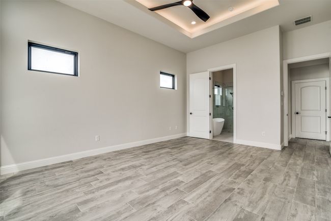 Unfurnished bedroom featuring light hardwood / wood-style floors, ensuite bathroom, ceiling fan, and a raised ceiling | Image 12