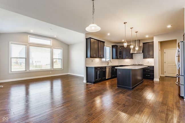 kitchen featuring vaulted ceiling, a center island, a sink, stainless steel appliances, and wall chimney exhaust hood | Image 17