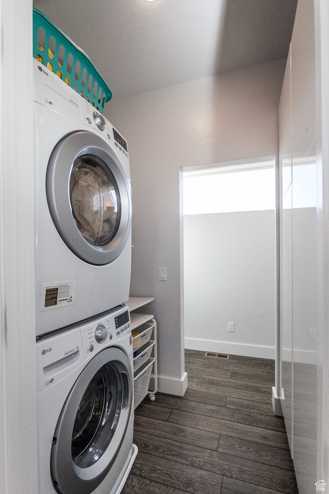 Clothes washing area with dark wood-style floors, stacked washer and clothes dryer, laundry area, and baseboards | Image 38