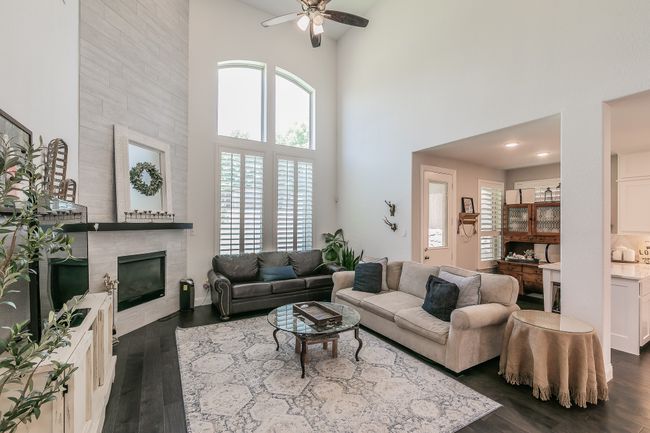 Living area featuring a high ceiling, ceiling fan, dark wood finished floors, a tile fireplace, and plenty of natural light | Image 10