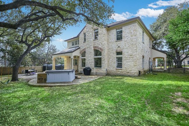 Rear view of house featuring stone siding, a fenced backyard, and a hot tub. | Image 36