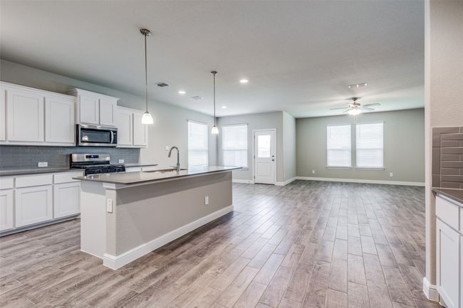 Kitchen with hanging light fixtures, appliances with stainless steel finishes, light hardwood / wood-style flooring, and a kitchen island with sink | Image 5
