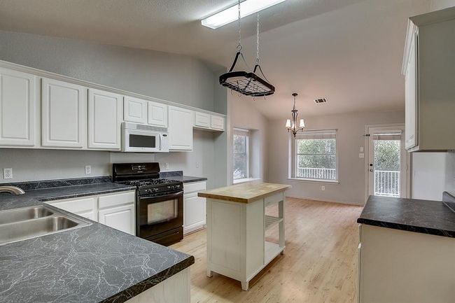 Kitchen with black gas range, white microwave, a sink, lofted ceiling, and white cabinetry | Image 9