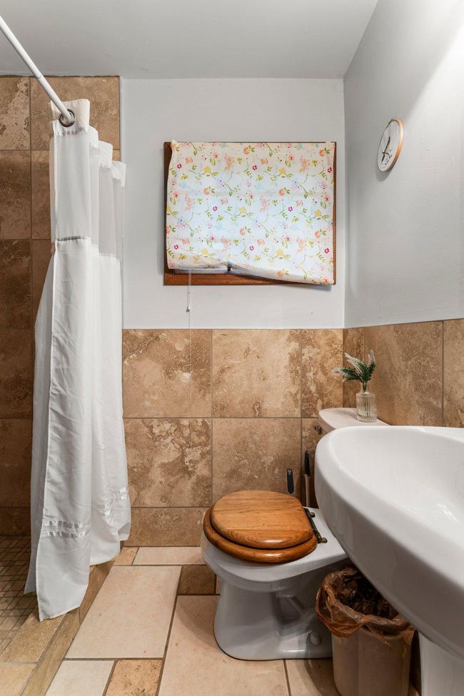 The ¾ bathroom features tiled flooring and wainscoting. There’s also a hallway with space for a stackable washer and dryer—offering added convenience for guests or tenants. | Image 22