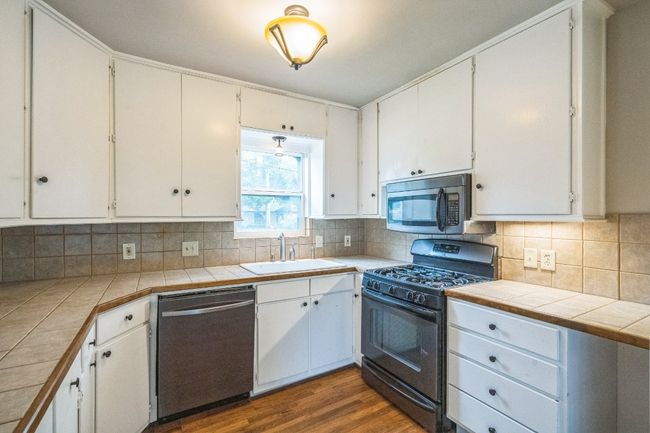Kitchen with stainless steel appliances, dark wood-style flooring, tasteful backsplash, white cabinetry, and tile counters | Image 7