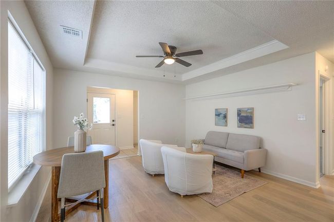 Living room with a textured ceiling, a raised ceiling, light wood-style flooring, and ceiling fan | Image 6