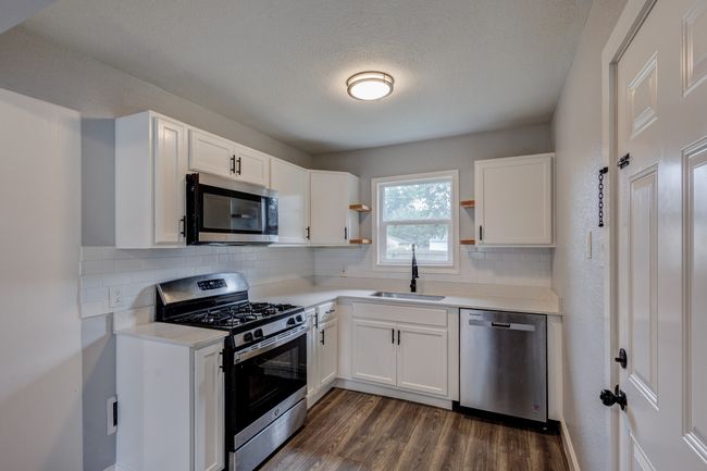 Kitchen featuring stainless steel appliances, open shelves, a sink, dark wood-style flooring, and white cabinetry | Image 5