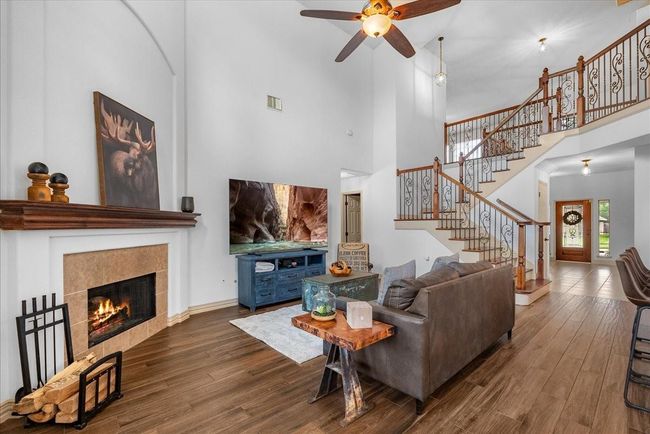 This inviting living room features high ceilings, a cozy fireplace, and elegant wooden flooring. A stylish staircase with ornate railings adds character, while large windows offer plenty of natural light. Ideal for relaxation and entertaining. | Image 17