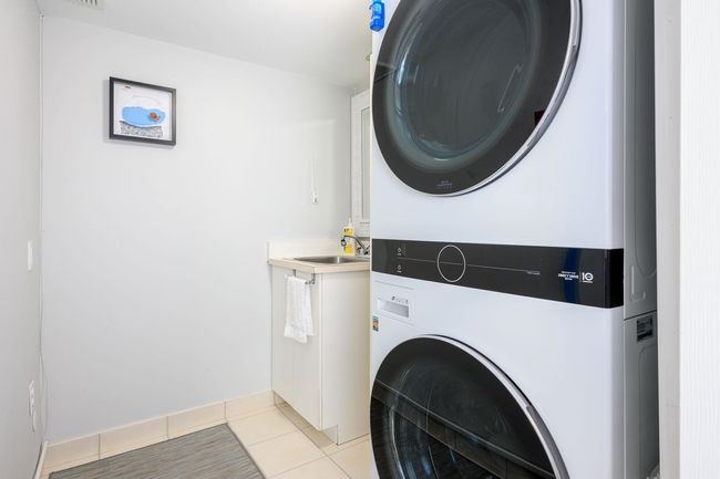 Laundry area with stacked washer / drying machine, light tile patterned flooring, and cabinet space | Image 26
