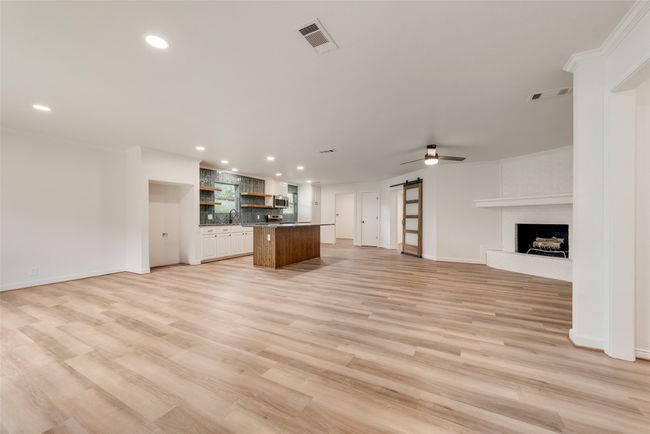 Unfurnished living room with recessed lighting, ceiling fan, a barn door, a fireplace, and light wood finished floors | Image 8