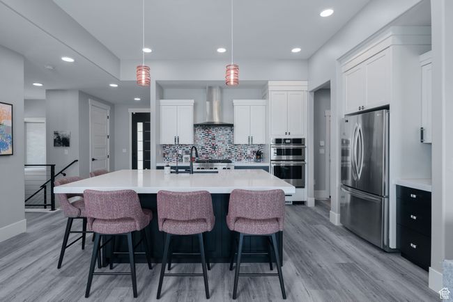 Kitchen featuring appliances with stainless steel finishes, wall chimney range hood, light wood-type flooring, a sink, and recessed lighting | Image 15